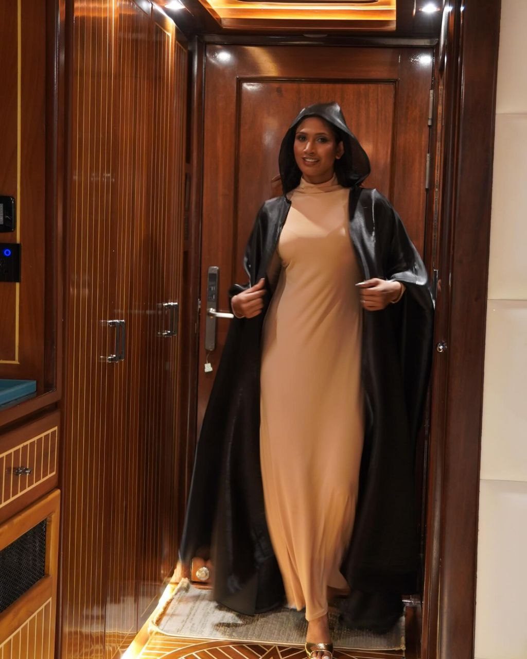 A woman in a metallic embellished Zuhair Murad evening gown with thin straps stands against a deep red background, exuding elegance.