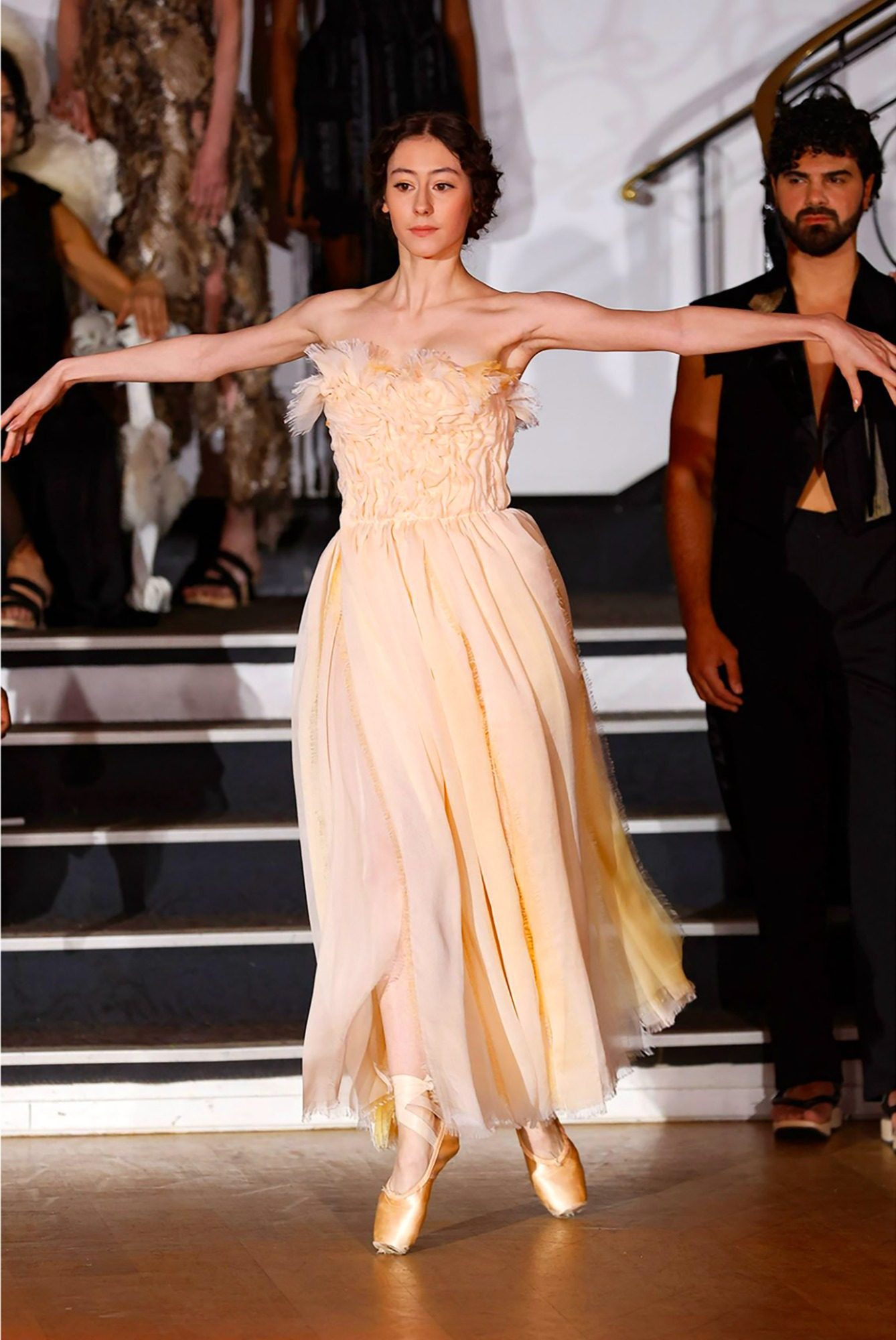 A woman in a metallic embellished Zuhair Murad evening gown with thin straps stands against a deep red background, exuding elegance.